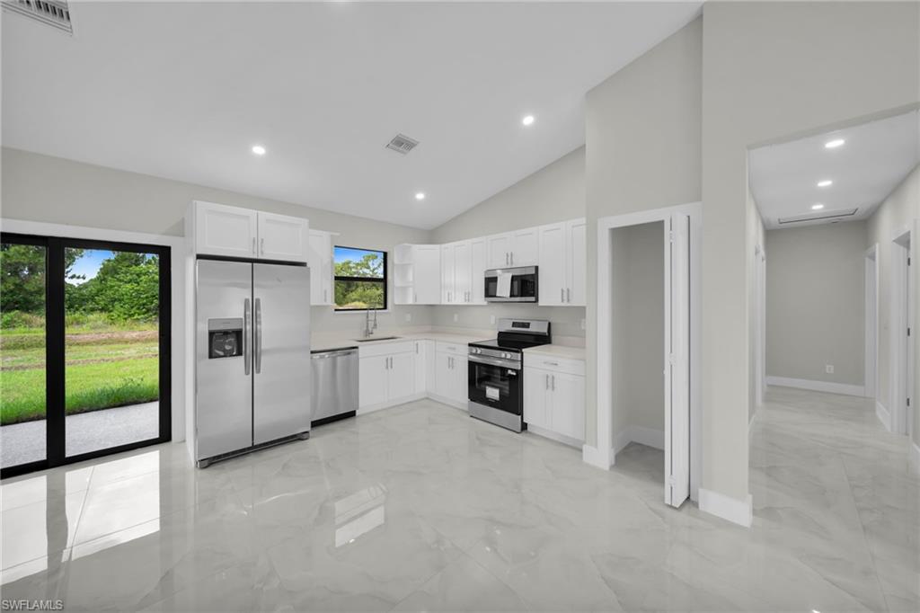 Kitchen featuring white shaker cabinetry, stainless steel appliances, light-toned countertops, and large format tile flooring