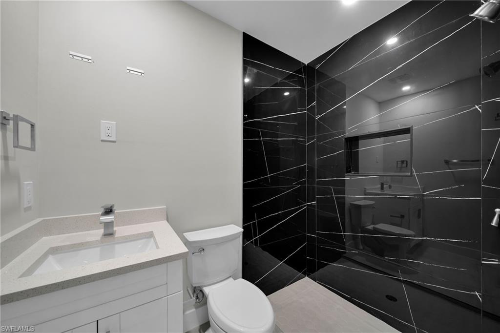 Contemporary bathroom featuring a black tiled shower with a niche, a white vanity with a light-colored countertop, and modern chrome fixtures