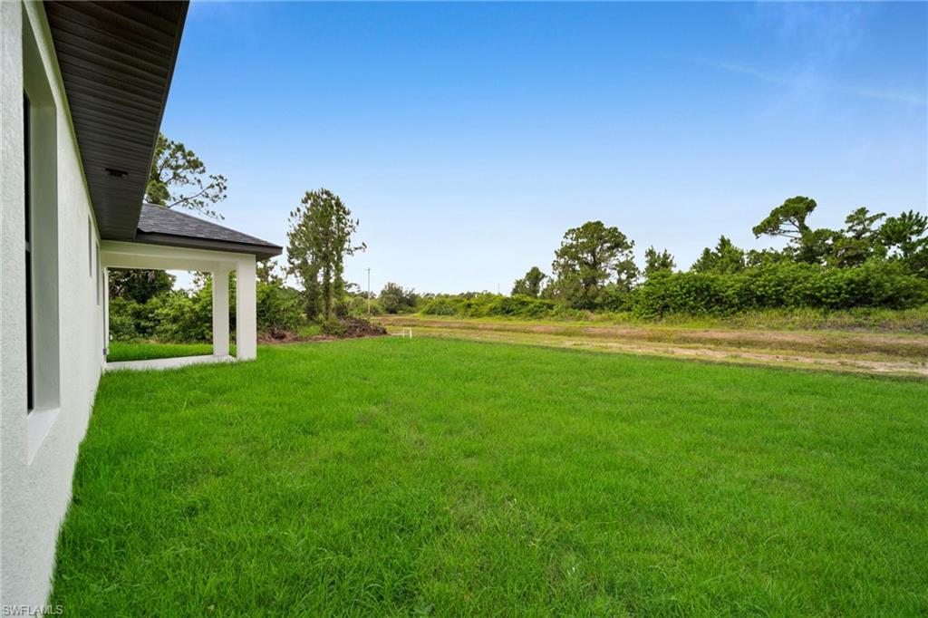 Expansive lawn area with a covered patio, new construction exterior, and a natural tree line bordering the property