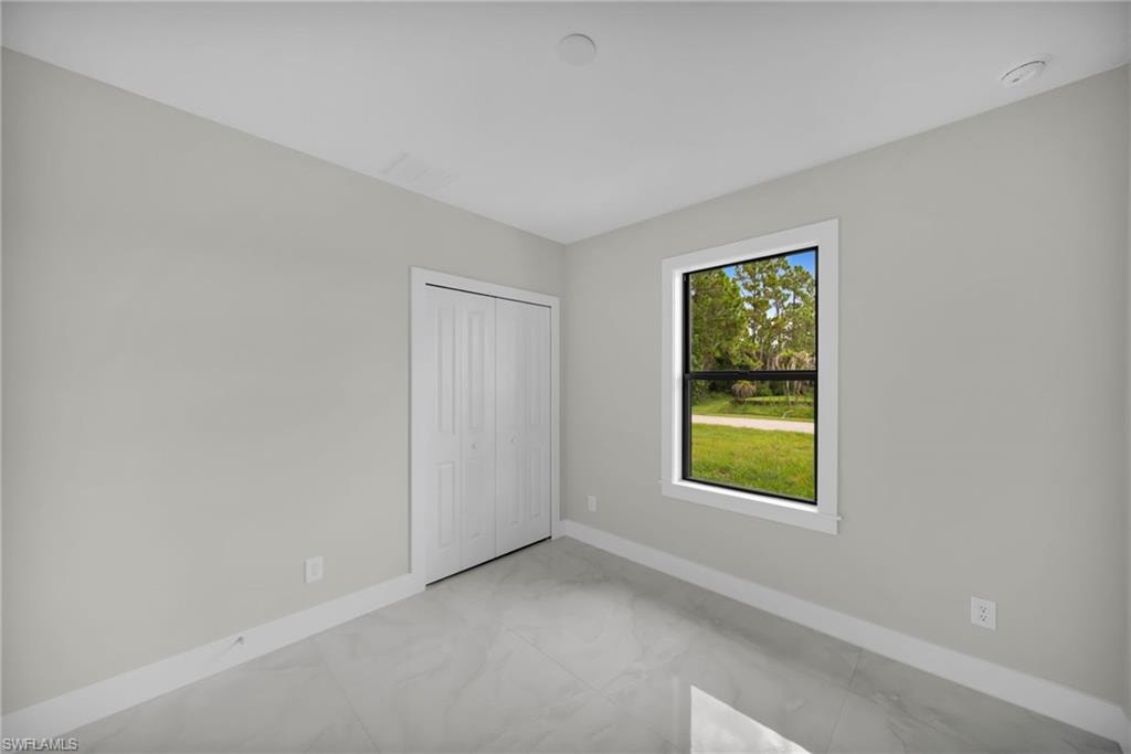 Room featuring a window with exterior landscaping, light gray walls, white baseboards, and bi-fold closet doors