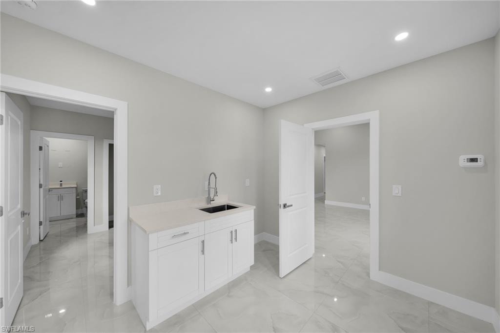 Wet bar featuring white cabinetry, a light-toned countertop, and a stainless steel sink with a gooseneck faucet