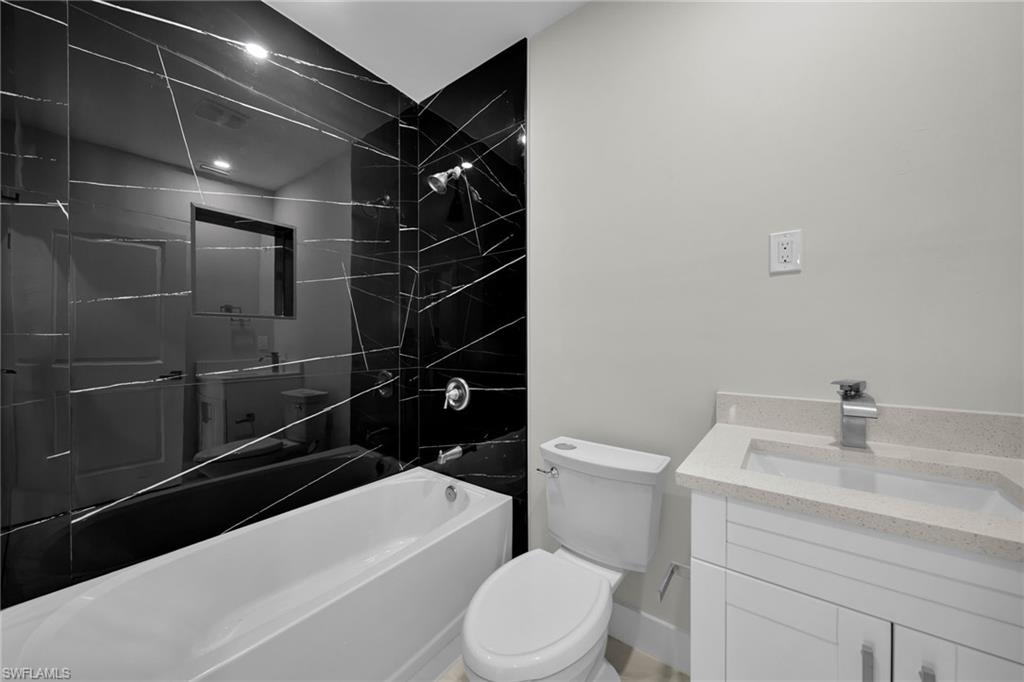 Bathroom featuring a black tiled shower surround with white veining, a white bathtub, a white vanity with a light-toned countertop, and a contemporary chrome faucet