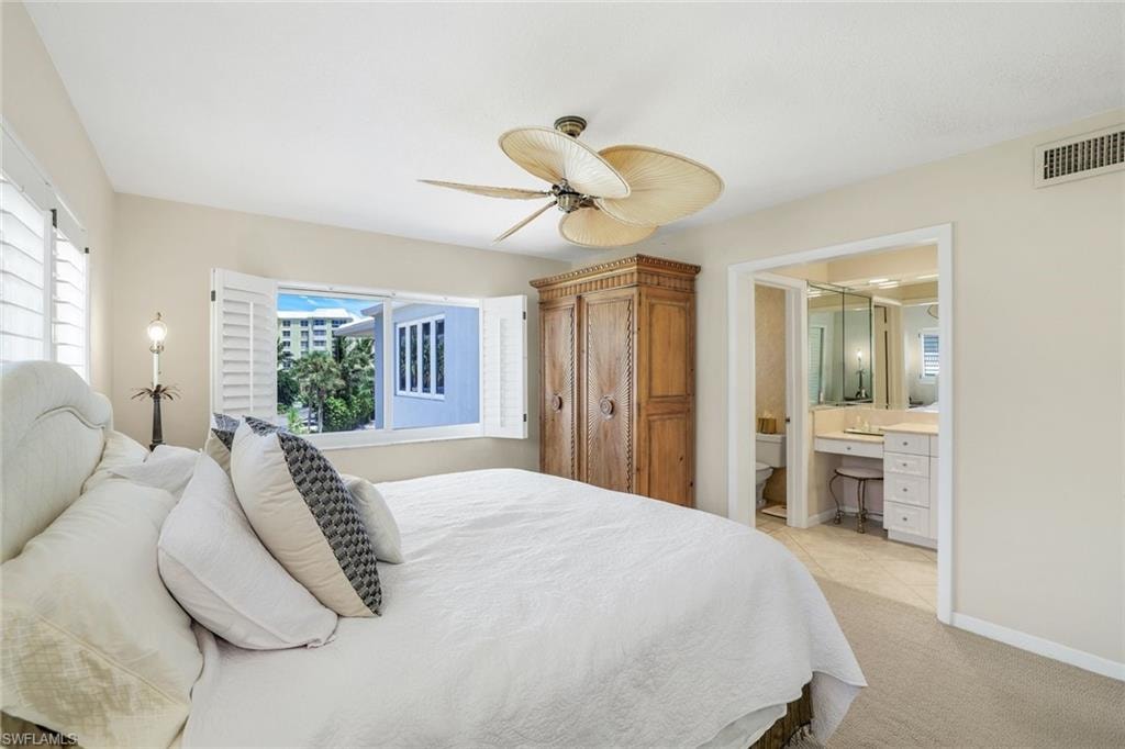Bedroom with built in study area, light carpet, ceiling fan, and connected bathroom
