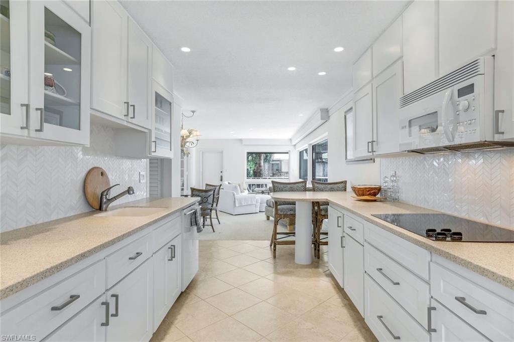 Kitchen featuring backsplash, white cabinetry, white microwave, glass insert cabinets, and recessed lighting