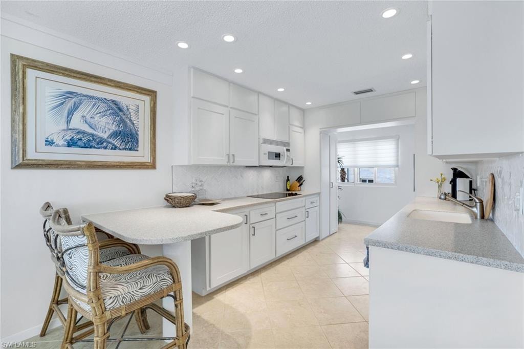 Kitchen with white cabinetry, a textured ceiling, backsplash, a peninsula, and recessed lighting