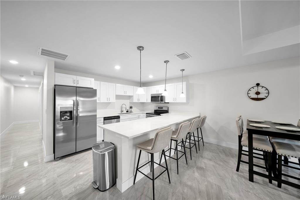 Contemporary kitchen featuring white cabinetry, stainless steel appliances, a long island with seating, pendant lighting, and light-toned tile flooring