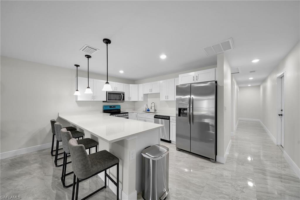 Spacious kitchen featuring an extended island with pendant lighting, white cabinetry, stainless steel appliances, and a tile backsplash