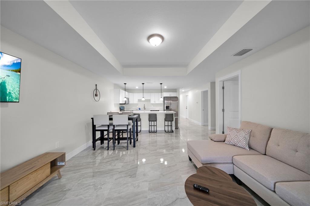 Open-concept living space featuring high ceilings, large format tile flooring, a dining area, and a kitchen with pendant lighting and stainless steel appliances