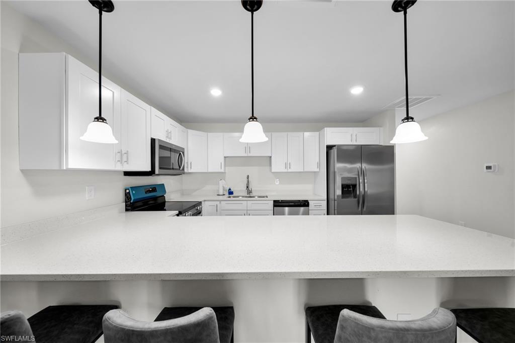 Kitchen featuring a spacious peninsula with pendant lighting, white cabinetry, integrated stainless steel appliances, and light-toned countertops
