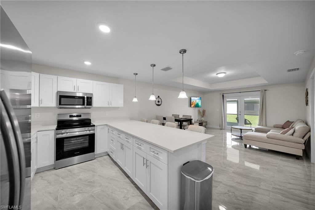 Open-concept living space featuring a kitchen island with pendant lighting, white cabinetry, stainless steel appliances, and large format tile flooring