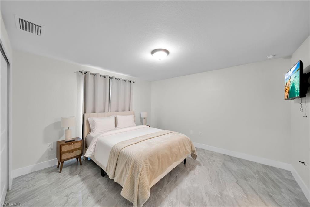 Spacious room featuring light-toned walls, contemporary ceiling light fixture, and grey wood-finish flooring
