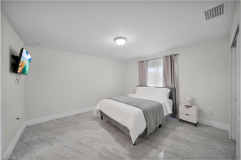 Spacious room featuring light-colored walls, tile flooring, and a window with curtains
