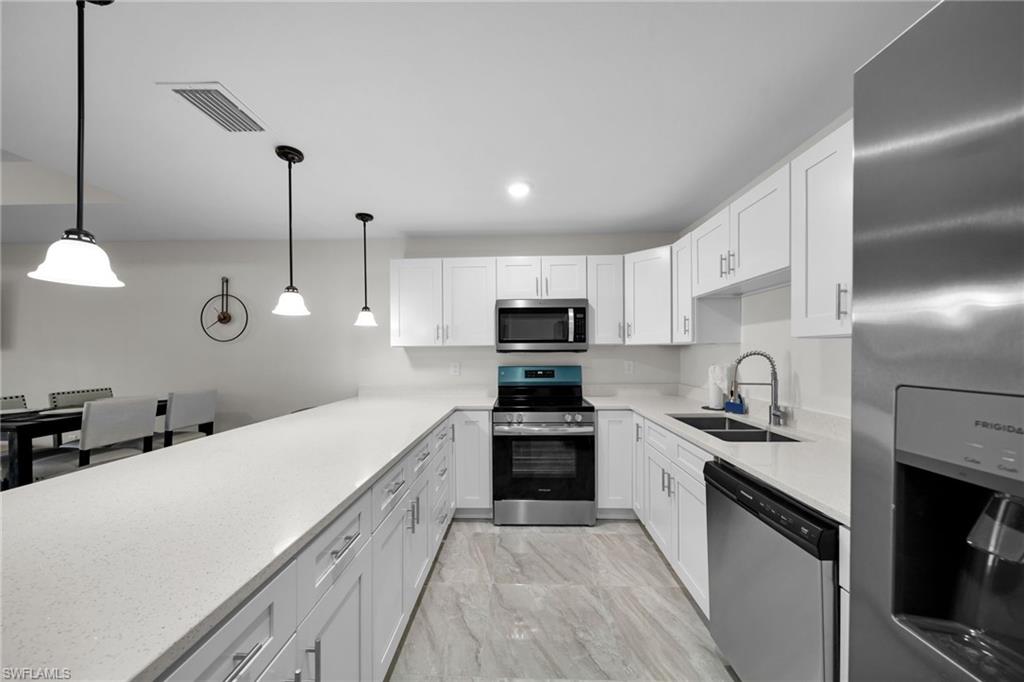 Modern kitchen featuring a spacious peninsula with light-toned countertops, white shaker cabinetry, stainless steel appliances, and pendant lighting