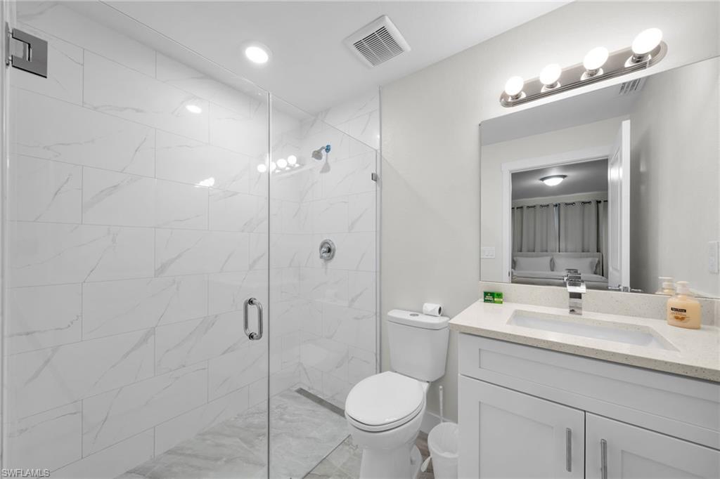 Bathroom featuring a glass-enclosed shower with large format tile, a white vanity with a quartz countertop, and a rectangular undermount sink