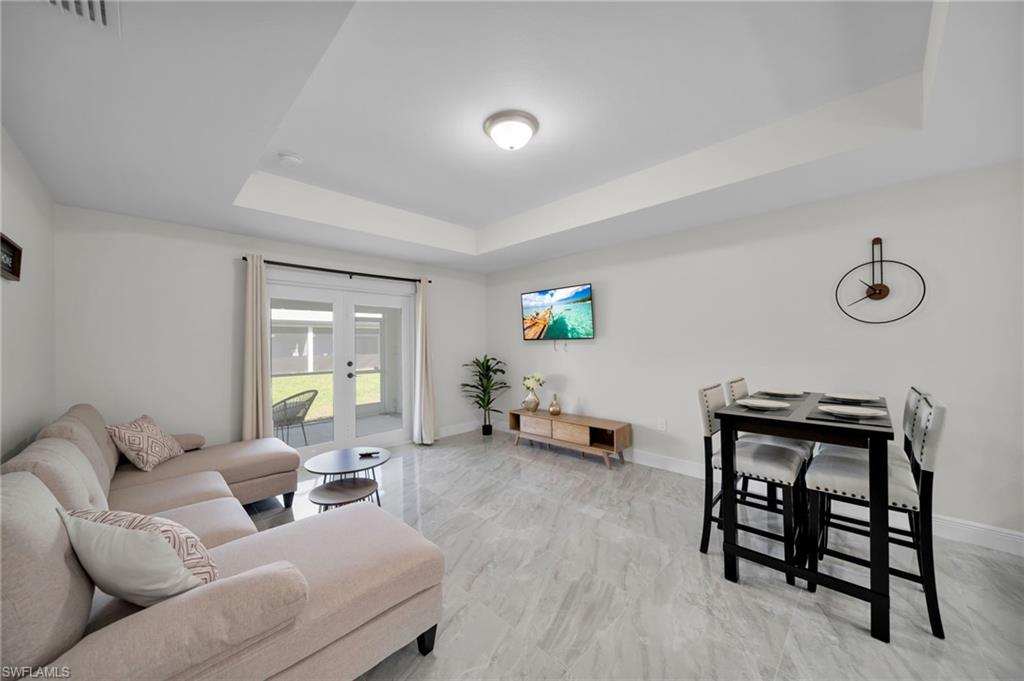 Bright living area featuring tray ceilings, wood-finish flooring, and direct access to an outdoor space through sliding glass doors