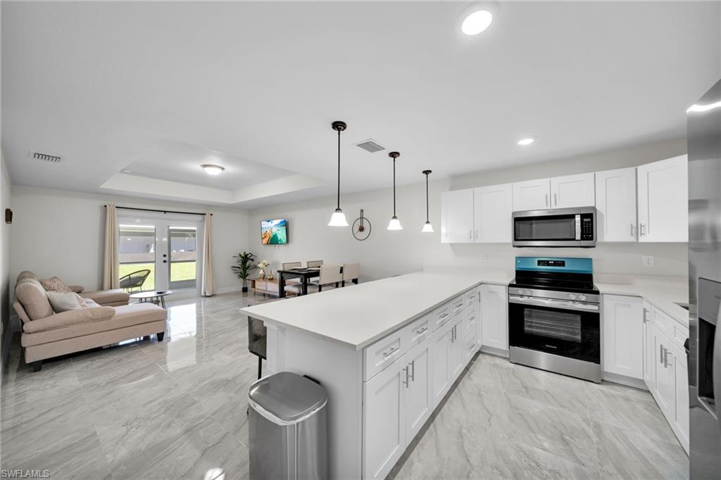 Modern kitchen featuring an expansive center island, white cabinetry, integrated stainless steel appliances, and pendant lighting