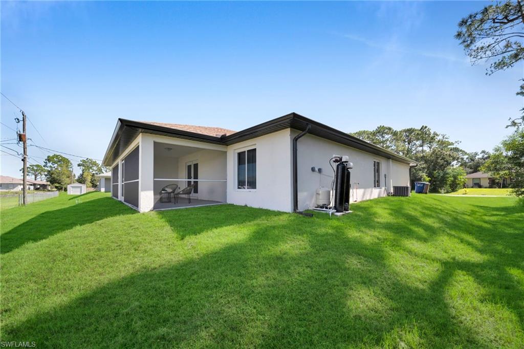 Expansive backyard featuring a screened-in patio, lush green lawn, and mature trees