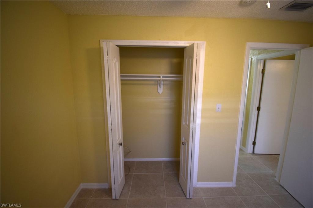 Interior room featuring a closet with bi-fold doors and a hanging rod, light tan wall paint, and square tile flooring