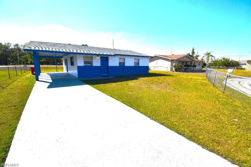 Single-story residence featuring a blue and white exterior, an attached carport, a paved driveway, and a chain-link fence