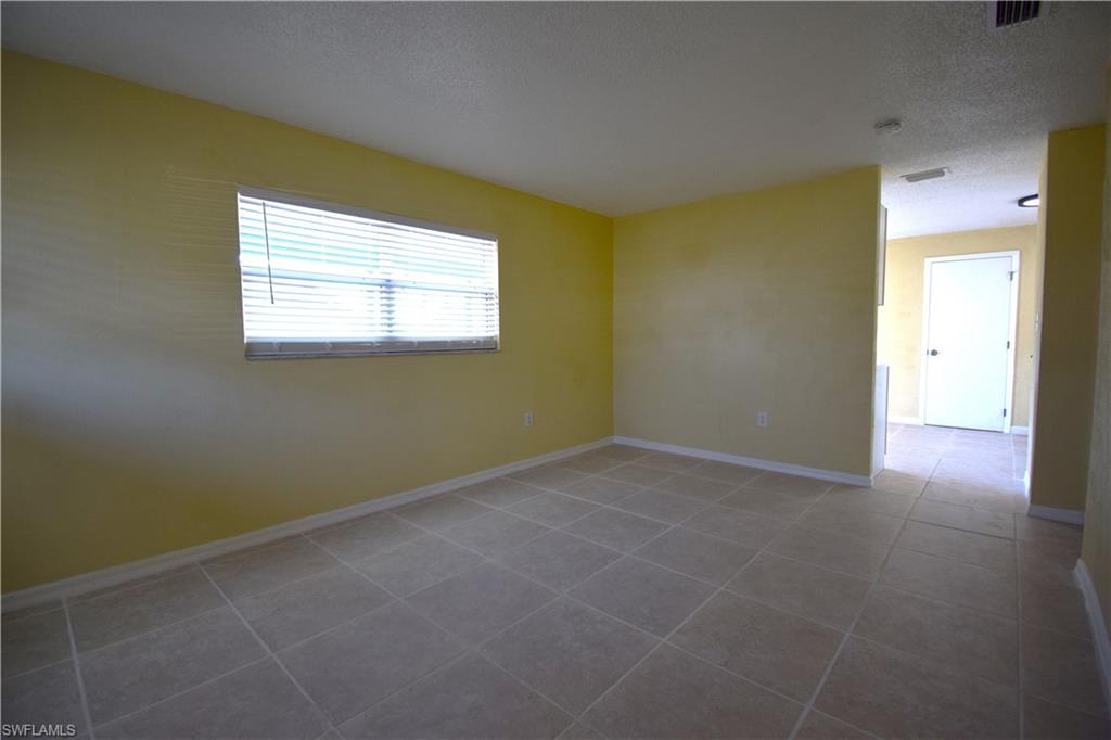 Spacious room featuring neutral tile flooring, a window with horizontal blinds, light yellow walls, and white baseboards