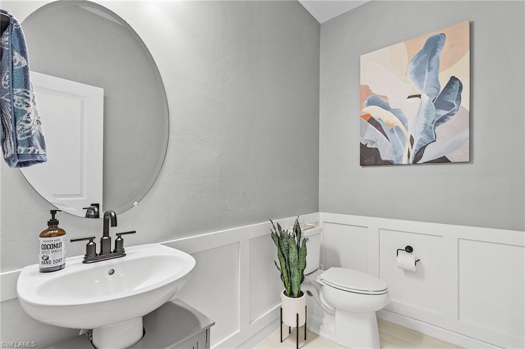 Powder room featuring a circular mirror, wall-mounted sink with dark bronze fixtures, wainscoting, and light gray wall paint