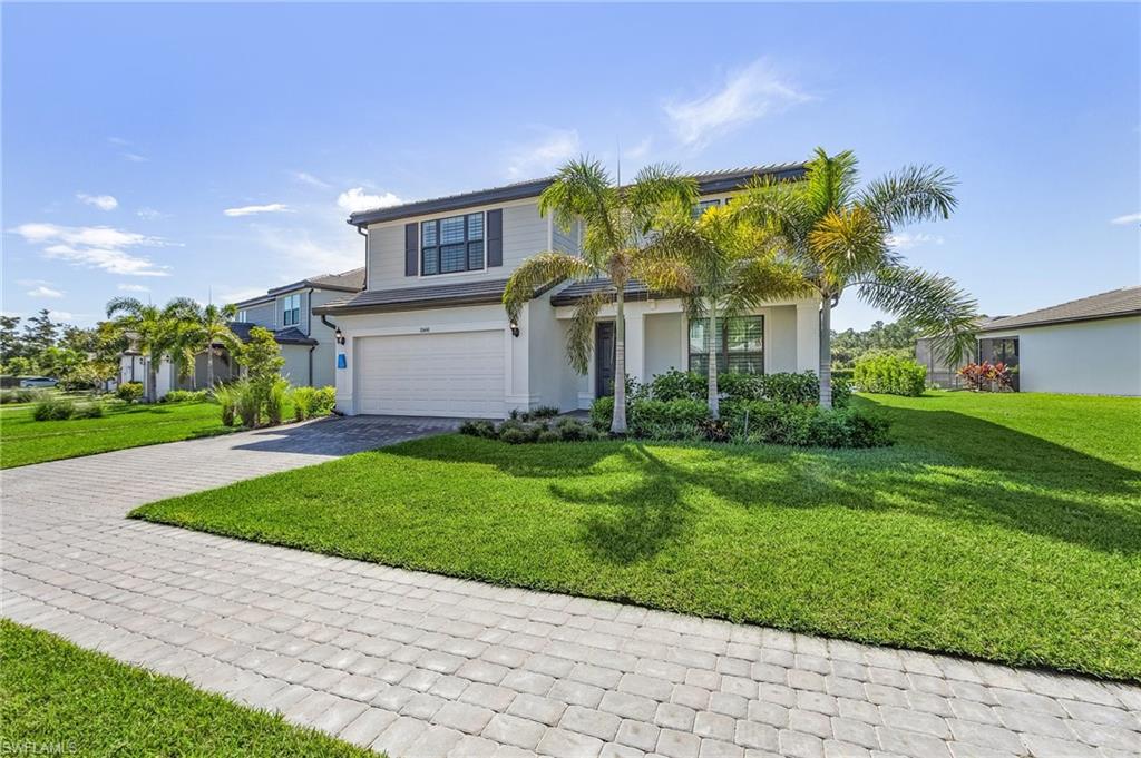 Two-story residence featuring a two-car garage, mature palm trees, and a paver driveway