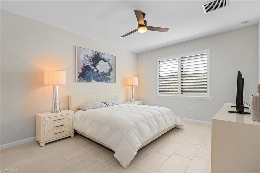 Light-toned rectangular tile flooring throughout, featuring a window with white plantation shutters, a ceiling fan with integrated lighting, and a neutral wall color