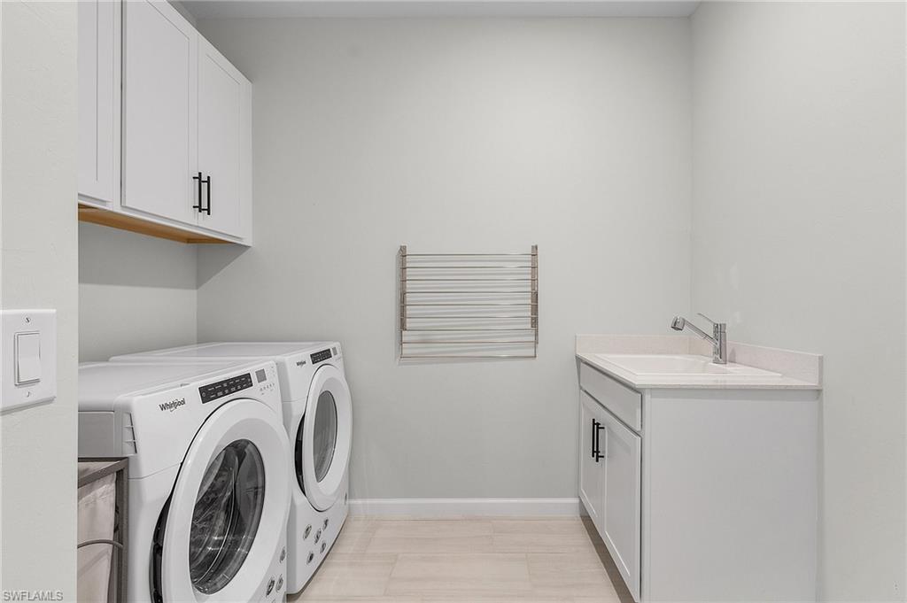 Laundry area featuring light wood-finish flooring, white cabinetry with dark hardware, a built-in sink with a chrome faucet, and a wall-mounted drying rack
