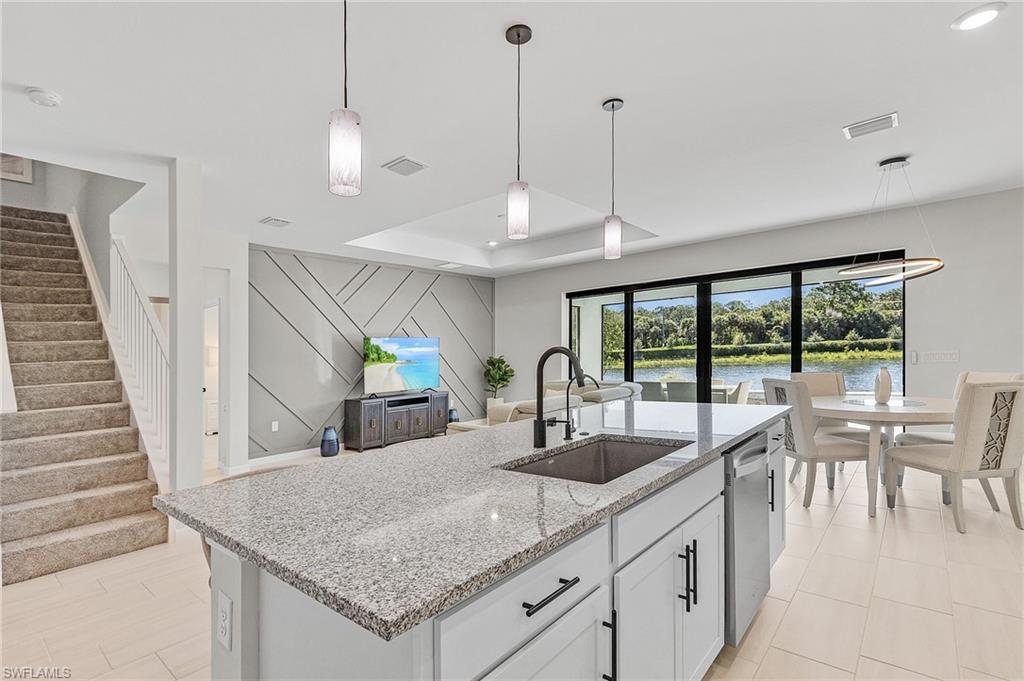 Open-concept living space featuring a central kitchen island with a granite-style countertop, white cabinetry with dark hardware, and a stainless steel sink with a dark faucet
