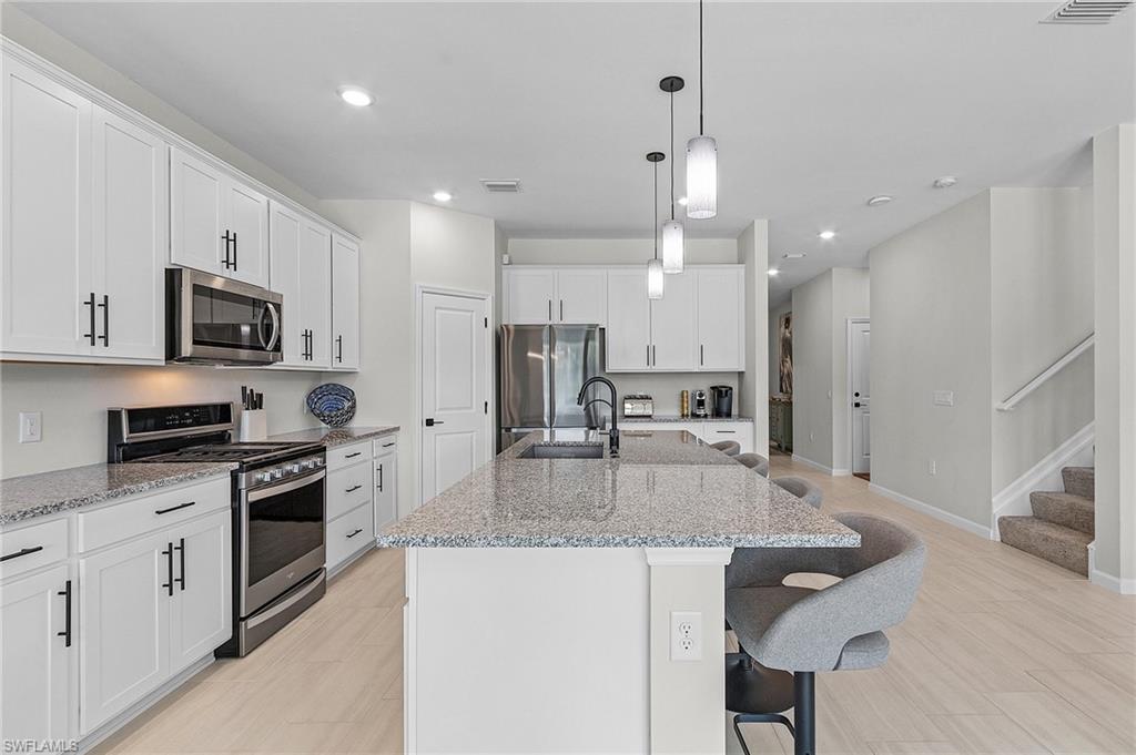 Contemporary kitchen featuring an oversized island with pendant lighting, stone countertops, white cabinetry with matte black hardware, stainless steel appliances, and wood-finish flooring