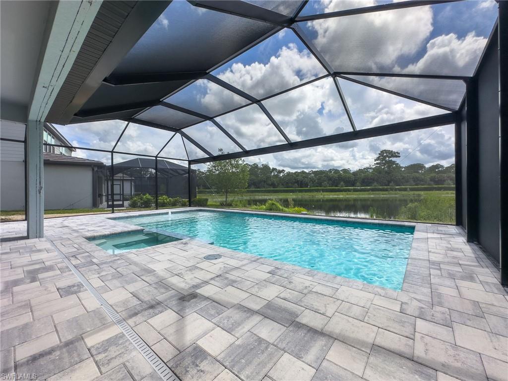 Screened-in pool deck featuring a rectangular swimming pool, integrated spa, and paver surfacing