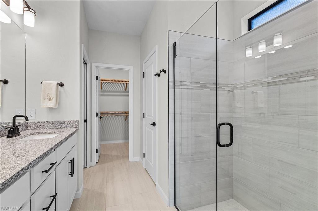 Modern bathroom featuring a glass-enclosed shower with tile surround, a single vanity with stone countertop, and light wood-finish flooring