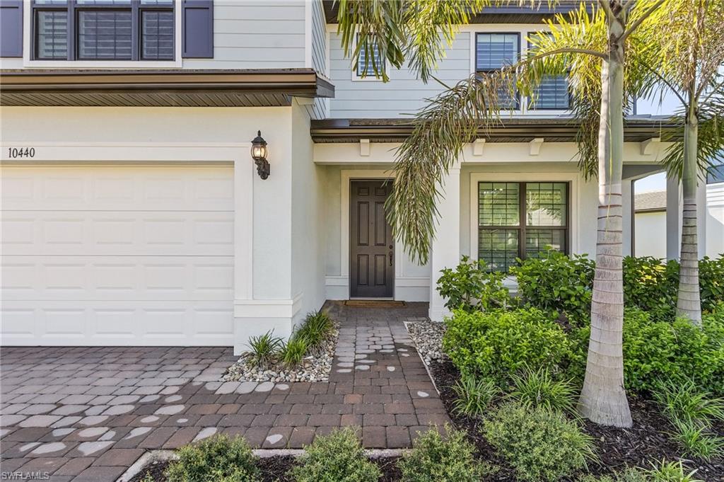 Exterior facade featuring a paneled garage door, paver driveway, dark-paneled entry door, mature palm trees, and established landscaping