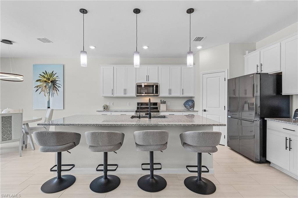 Gourmet kitchen featuring a large island with granite countertops, pendant lighting, white shaker cabinetry, and stainless-steel appliances