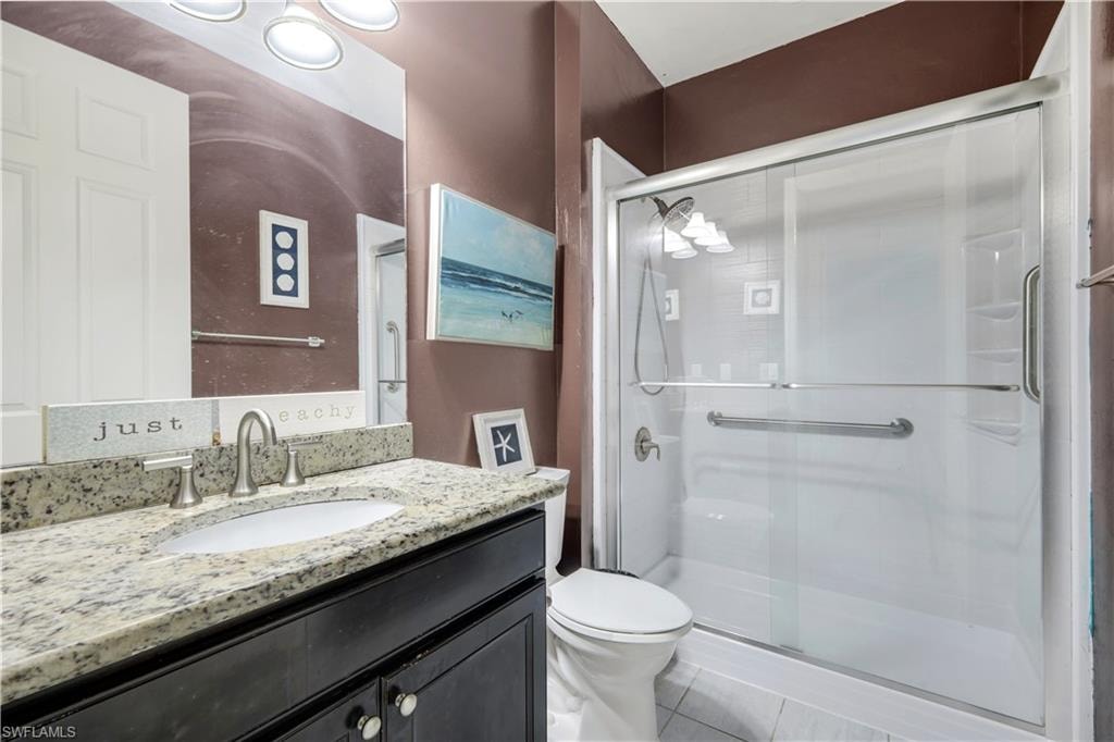 Bathroom featuring a dark wood-finish vanity with a granite countertop and undermount sink, a chrome faucet, and a glass-enclosed shower with grab bars and a white tile floor