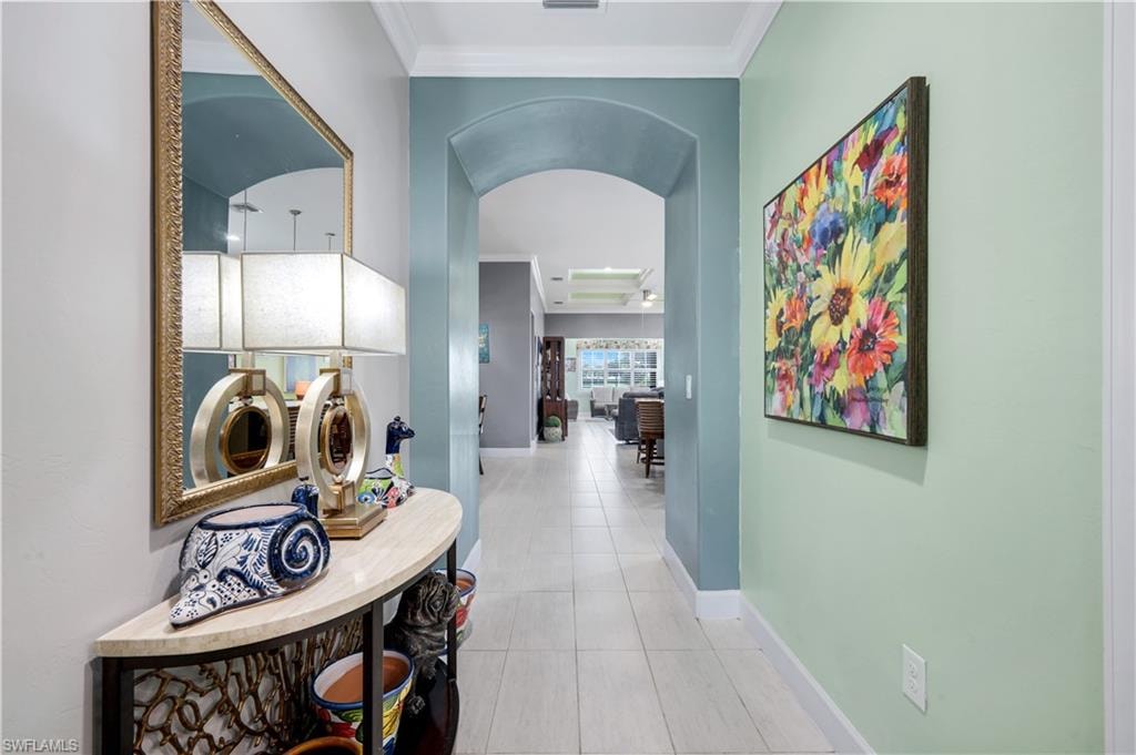Tiled hallway featuring an arched entryway, crown molding, and light-toned walls