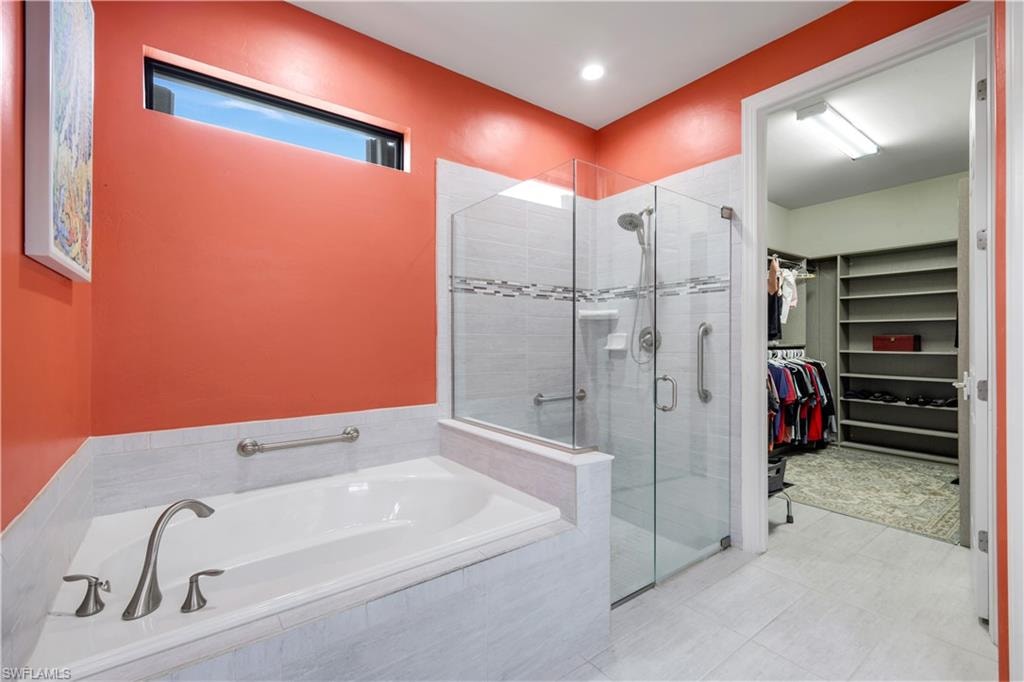 Spacious bathroom featuring a built-in tub, a glass-enclosed shower with tiled walls and a mosaic accent, and a doorway leading to a walk-in closet with custom built-in shelving