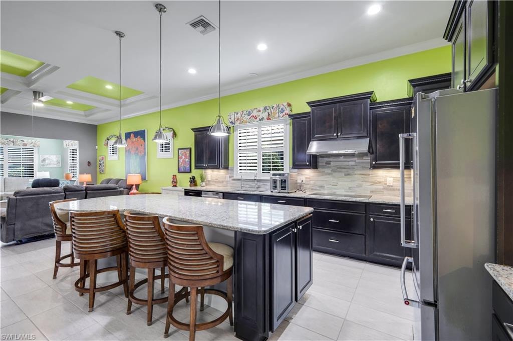 Modern kitchen featuring dark wood cabinetry, updated stainless steel appliances, a tiled backsplash, and a large granite countertop island with pendant lighting