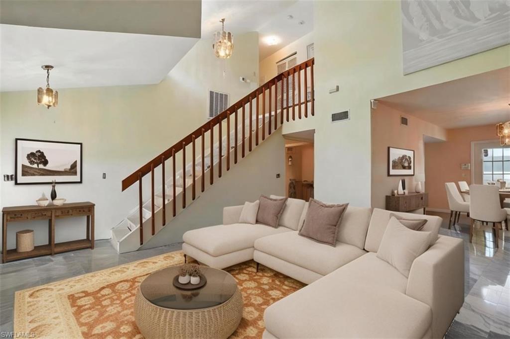 Living room featuring a chandelier, marble finish flooring, a towering ceiling, and stairs - Virtually Stage and Edited Image