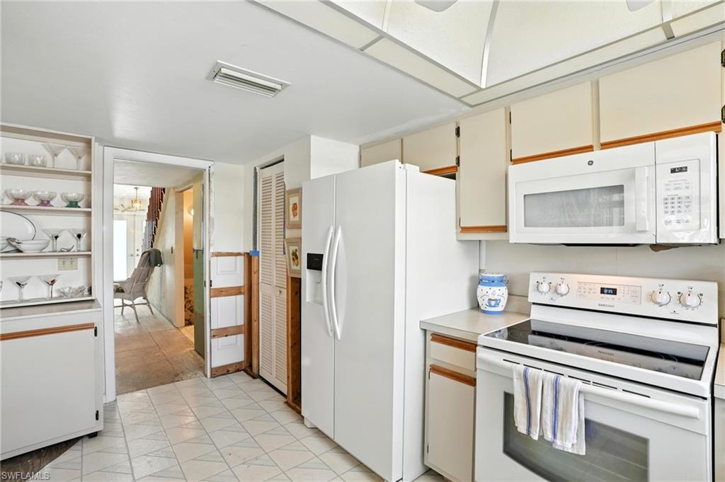 Kitchen featuring white appliances, light countertops, cream cabinets, and open shelves - Virtually Edited Image
