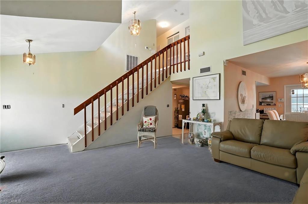 Carpeted living area with a chandelier, a high ceiling, and stairway - Virtually Edited Image