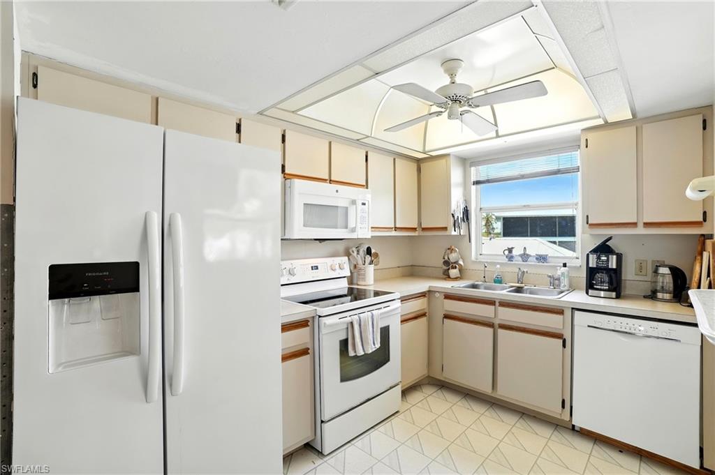 Kitchen featuring white appliances, cream cabinetry, light countertops, and a ceiling fan - Virtually Edited Image