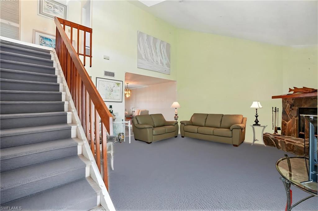 Living room with a fireplace, carpet, stairs, and a high ceiling - Virtually Edited Image