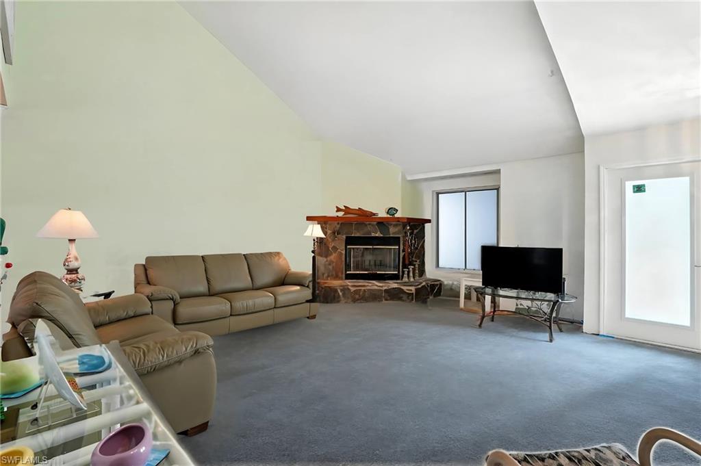 Living area featuring a fireplace, lofted ceiling, and carpet flooring - Virtually Edited Image
