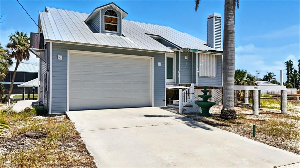 View of front facade featuring concrete driveway, a chimney, and a metal roof - Virtually Edited Image