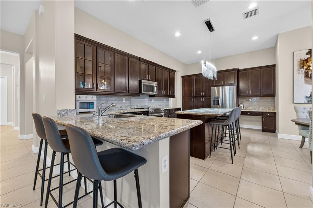 Kitchen featuring granite countertops, dark wood cabinetry, stainless steel appliances, and tile flooring
