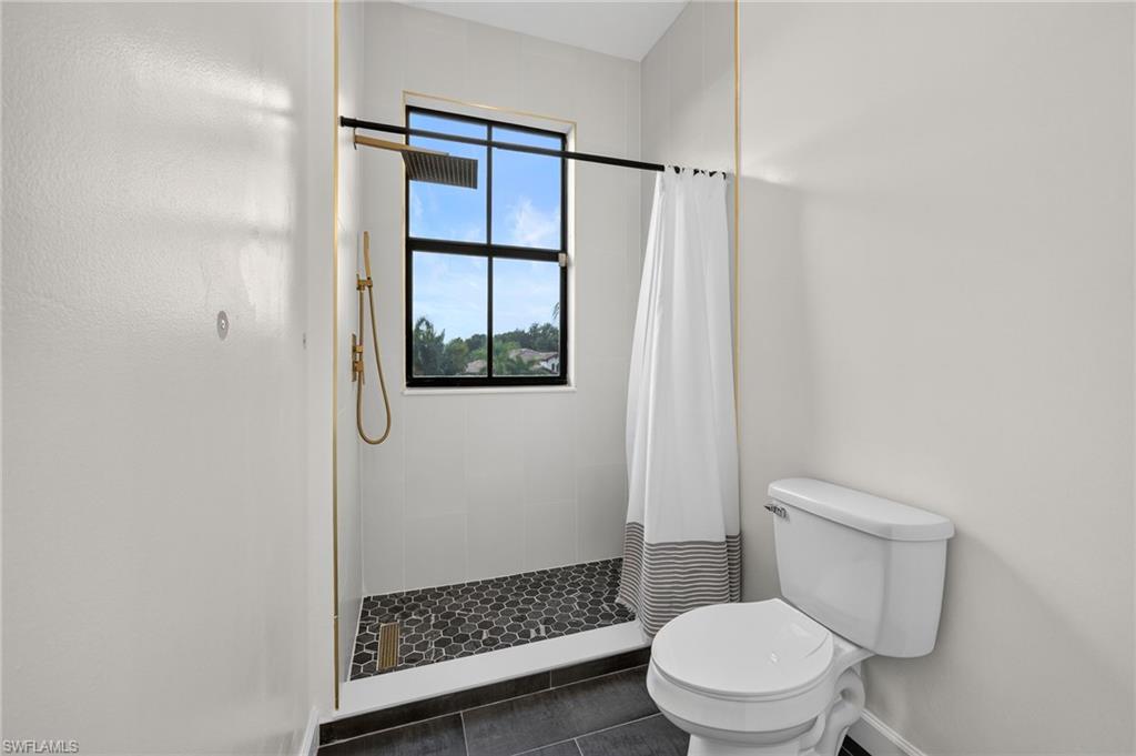 Walk-in shower featuring black hexagon tile flooring, and gold finishes