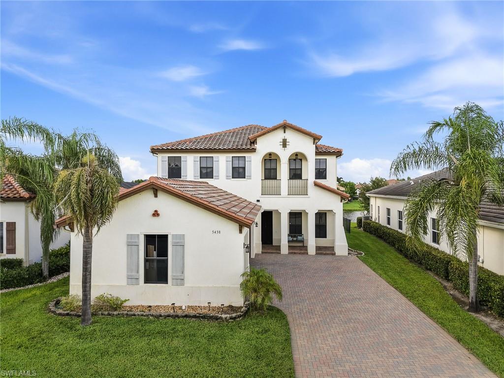 Mediterranean Revival architectural style with a tile roof, stucco exterior, decorative arched entryway, and a paver driveway