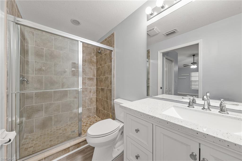 Bathroom featuring a tiled walk-in shower with glass enclosure, white vanity with integrated sink, speckled countertop, and wall-mounted mirror