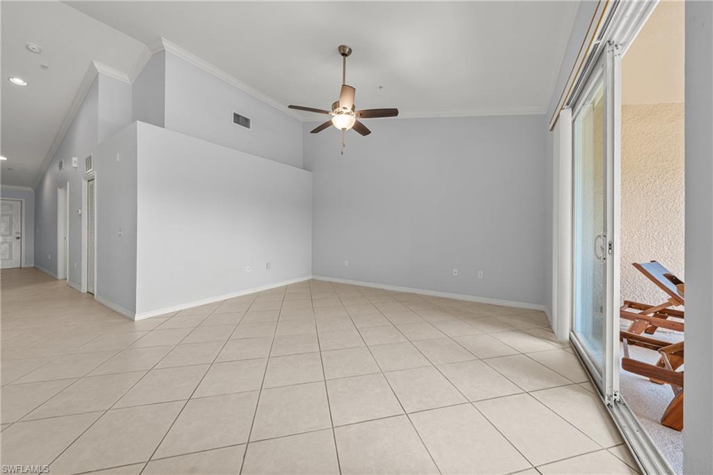 Spacious interior room featuring light-colored tile flooring, crown molding, a ceiling fan, and a large sliding glass door opening to an outdoor patio area